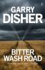 The book cover of Bitter Wash Road by Garry Disher showing a dried out wheat field with two tyre tracks running through it, echoed by a hint of light against a dark cloudy sky. There&#039;s a quote &#039;Bitter Wash Road is superb.&#039; The Australian.