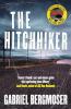 The book cover of The Hitchhiker by Gabriel Bergmoser has a yellow &quot;sticker&quot; on the front that says Bestselling Author, Must-Read Suspense, with part of the book cover and the title of The Caretaker in the middle. There&#039;s also a quote at the bottom &#039;I haven&#039;t found a cat-and-mouse game this captivating since Misery.&#039; Jack Heath, author of Kill Your Husbands.

The image is of a long, rough country road with electricity poles running alongside it, and a rail crossing right in front. There are fields off to the side, and a car barely visible through the dust it is kicking up. Overhead, a cloudy, grey and white vast sky.